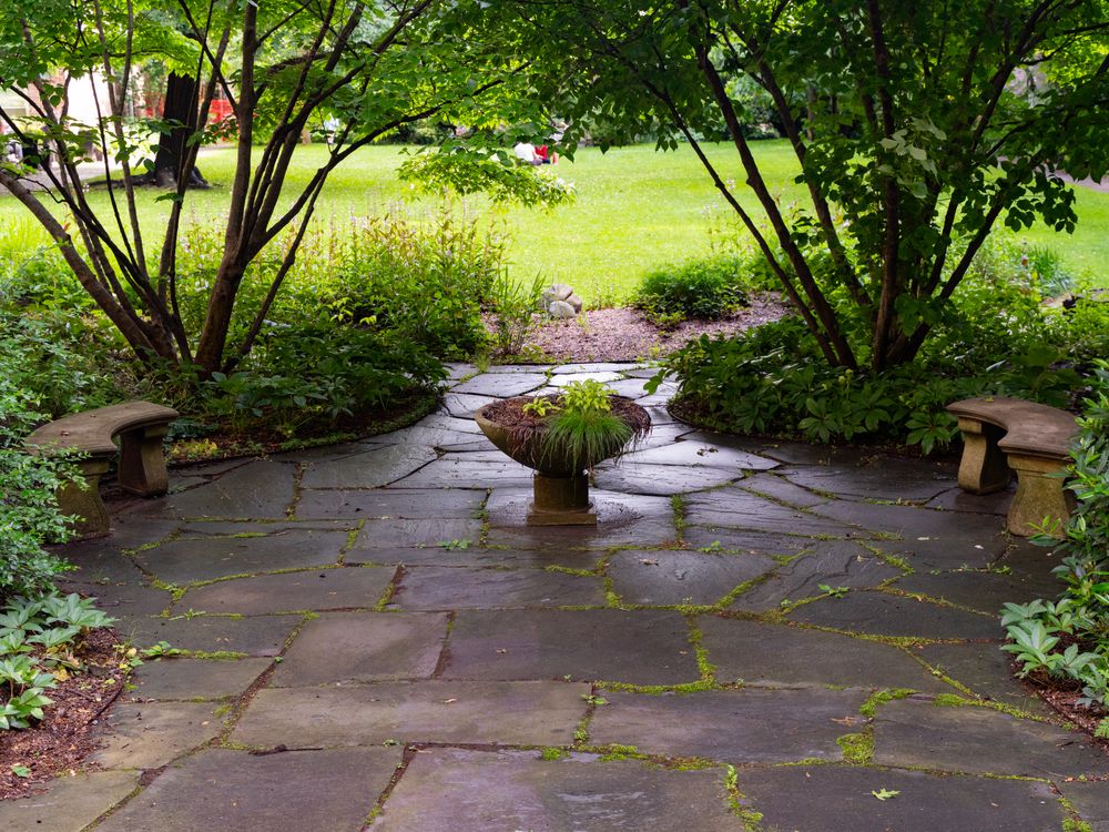 Flagstone garden path leading through a shaded perennial border to a stone planter